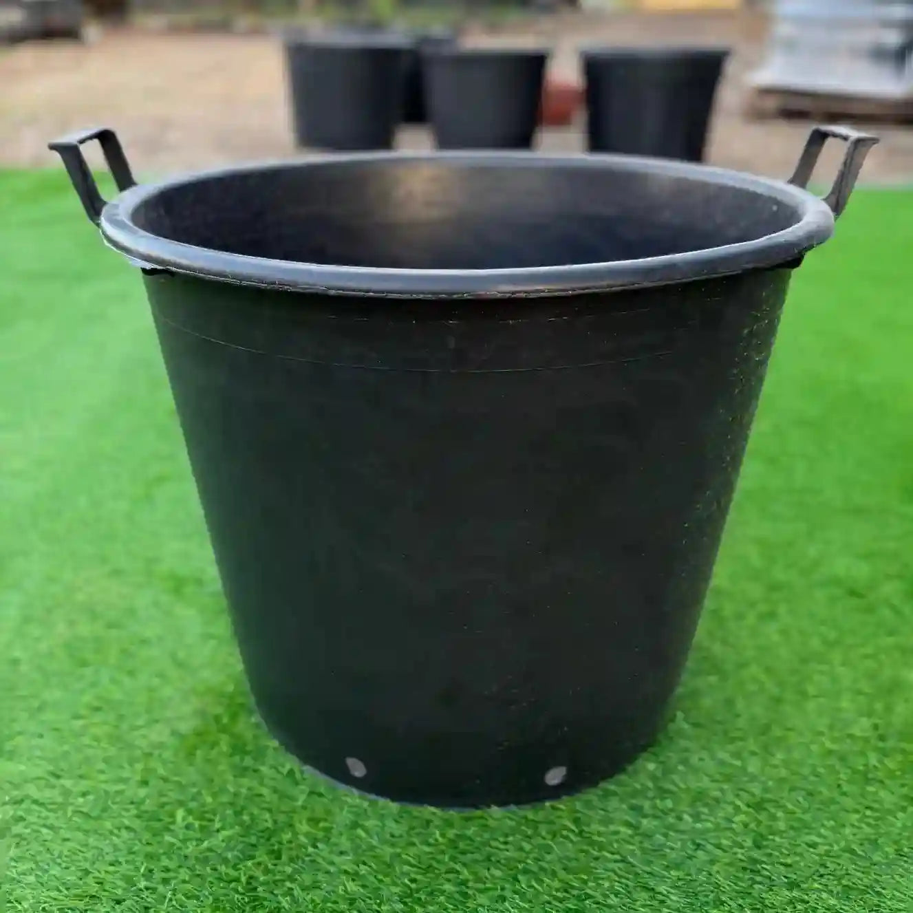 Black plastic bucket on a green grass background