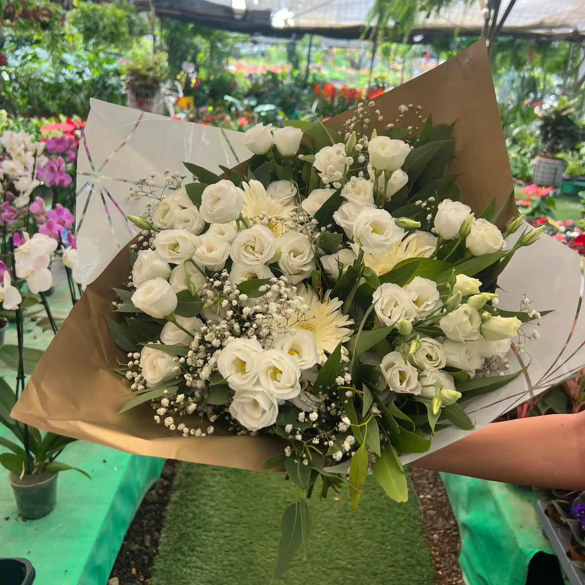Bouquet of white flowers held by a person in a greenhouse setting